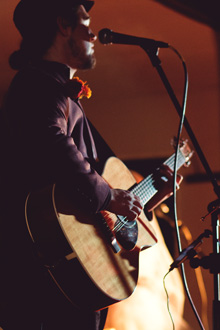 He is poised at his focused guitar, the flower at his lapel glowing orange