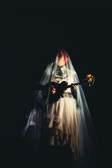 She is shrouded in white, underneath the veil, her hands playing the darkened mandolin
